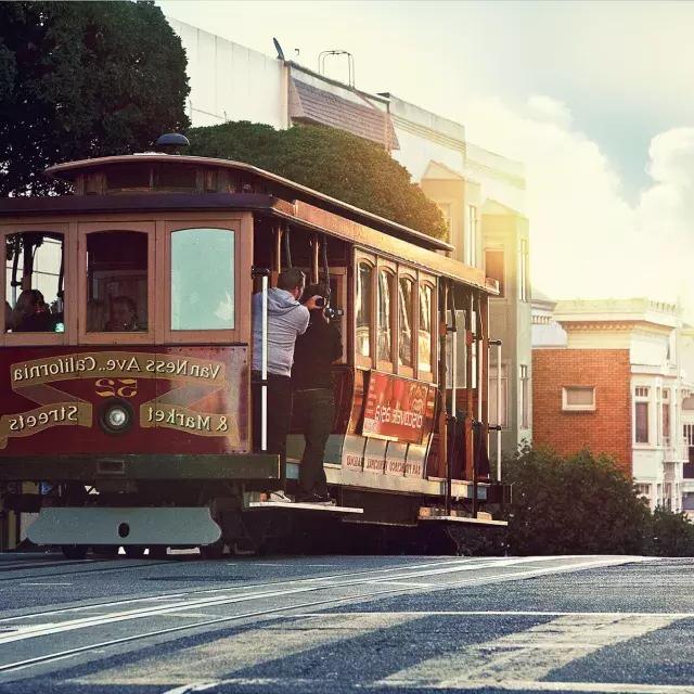 A 缆车 rounds a hill in San Francisco with passengers looking out the window.